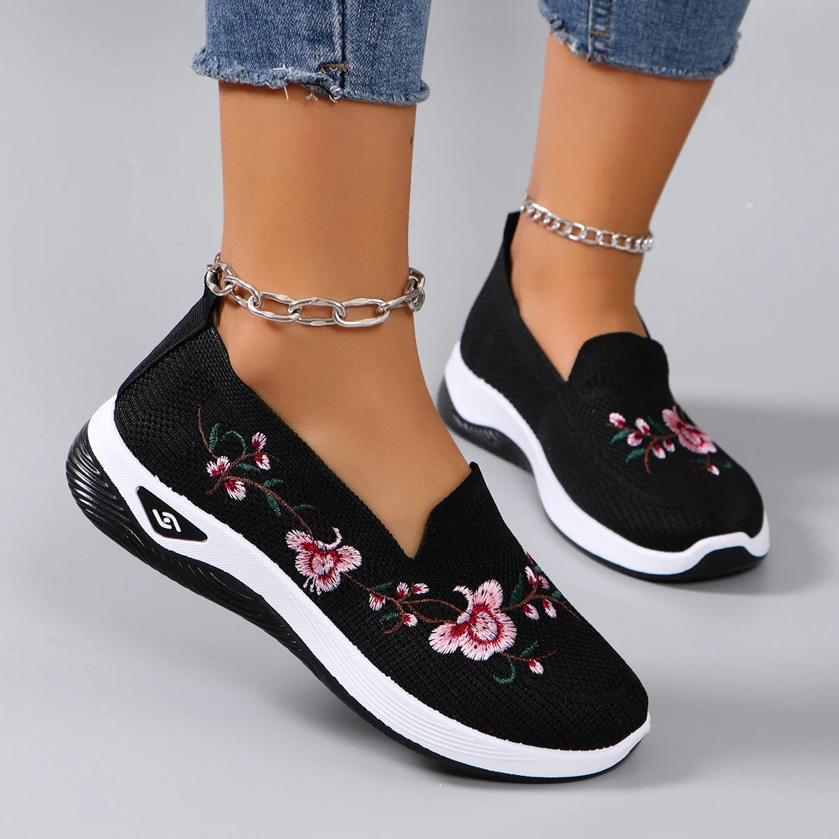 Black slip-on sneakers with floral embroidery on a gray background