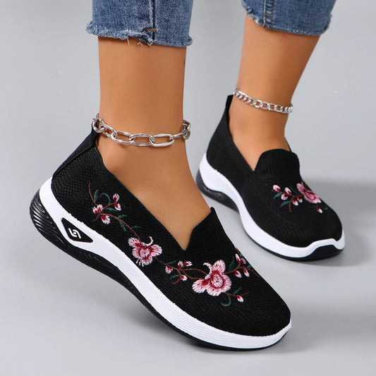 Black slip-on sneakers with floral embroidery on a gray background