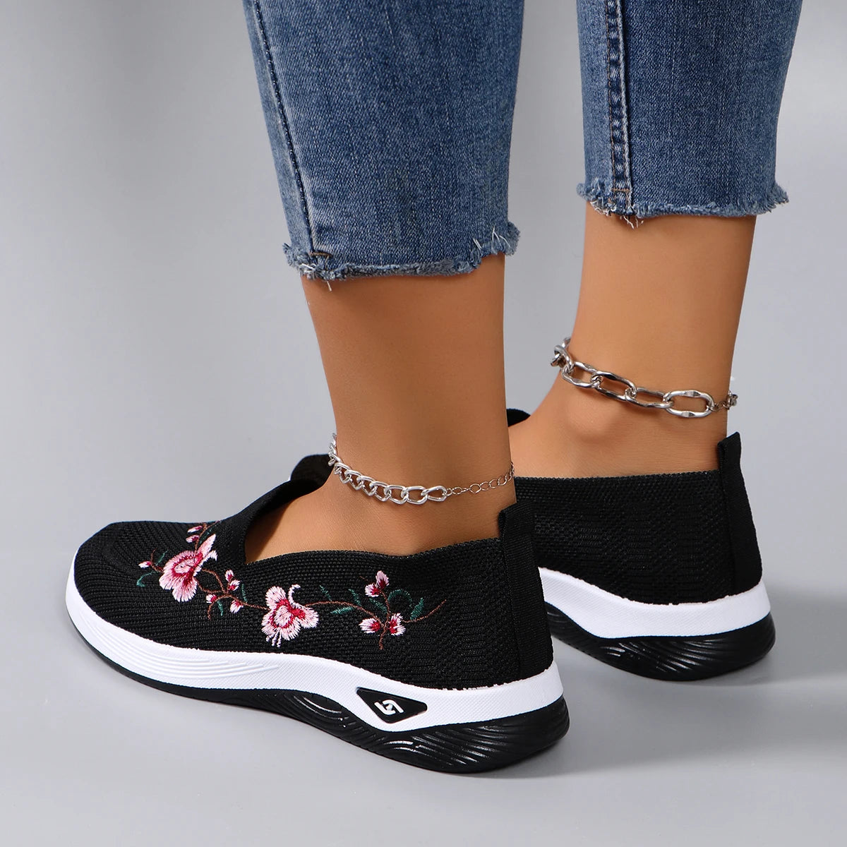 Black slip-on sneakers with floral design worn with blue jeans on a gray background
