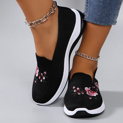 Black slip-on sneakers with floral embroidery on a gray background