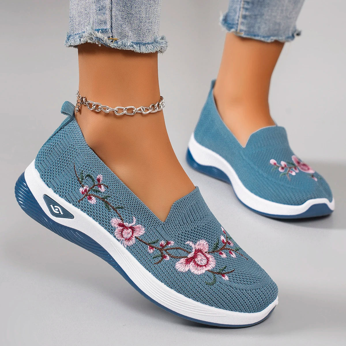 Blue embroidered shoes worn with denim jeans on a gray background