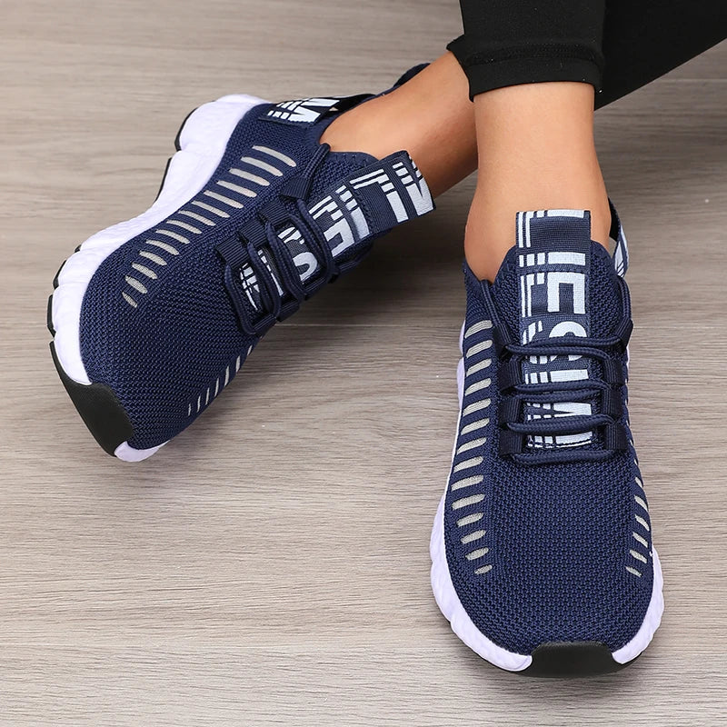 Navy blue athletic shoes with white accents worn by a person on a wooden floor.
