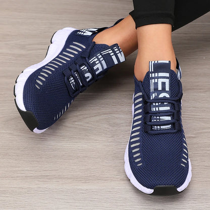 Navy blue athletic shoes with white accents worn by a person on a wooden floor.