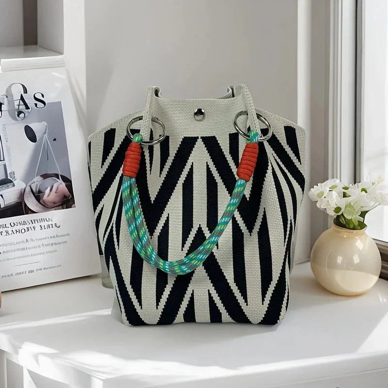 Black and white patterned handbag with colorful handles on a white surface.