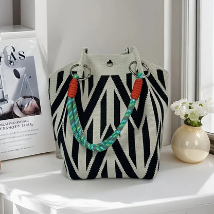Black and white patterned handbag with colorful handles on a white surface.
