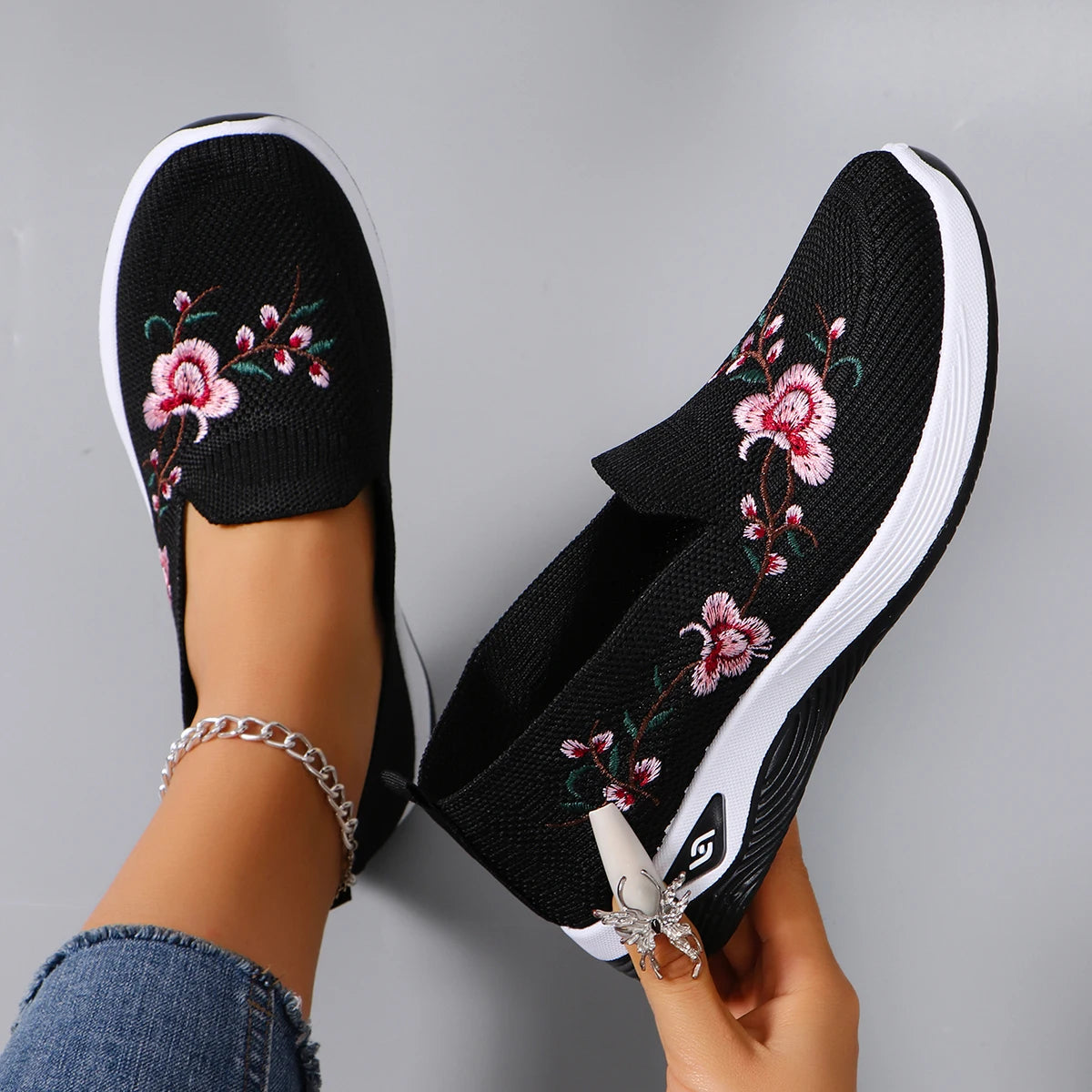 Black slip-on shoes with floral embroidery on a gray background