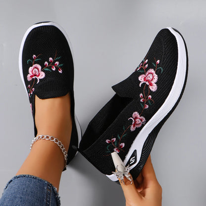 Black slip-on shoes with floral embroidery on a gray background